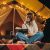 Smiling Woman Freelancer Drinking Wine And Read Book Sitting In Cozy Glamping Tent In Autumn Evening. Luxury Camping Tent For Outdoor Holiday And Vacation. Lifestyle Concept