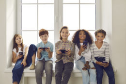 Happy Multiethnic Children Playing Games On Mobile Phones Sitting On Windowsill