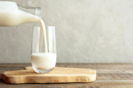 Kefir, Milk Or Turkish Ayran Drink Are Poured Into A Glass Cup From A Bottle. A Glass Stands On A Wooden Stand On A Rustic Wooden Table. Place For Text