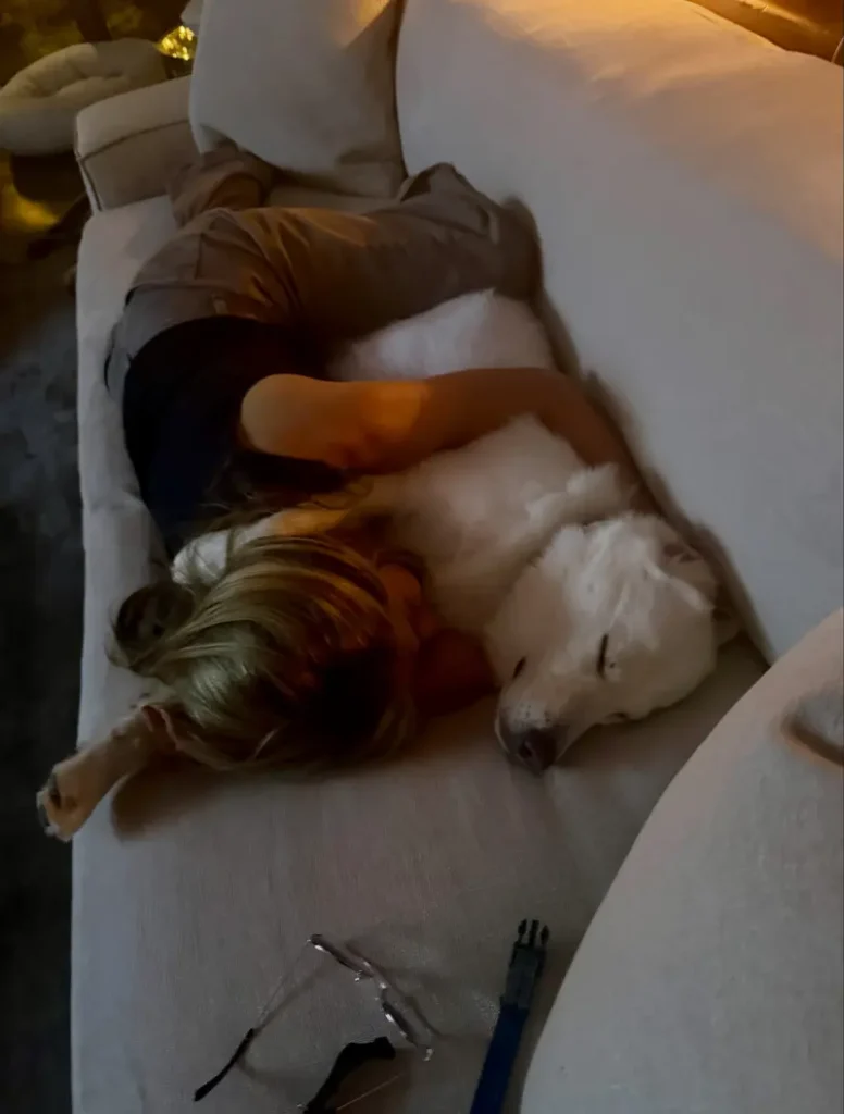 Jennifer Aniston a kutyájával egy kanapén, barna farmerben